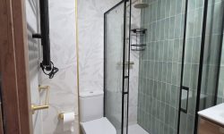 Baño moderno reformado con dos tipos de azulejos, ducha y mampara negra.