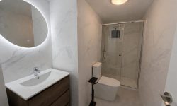 Baño moderno y acogedor con marmolados blanco espejo redondo y plato de ducha
