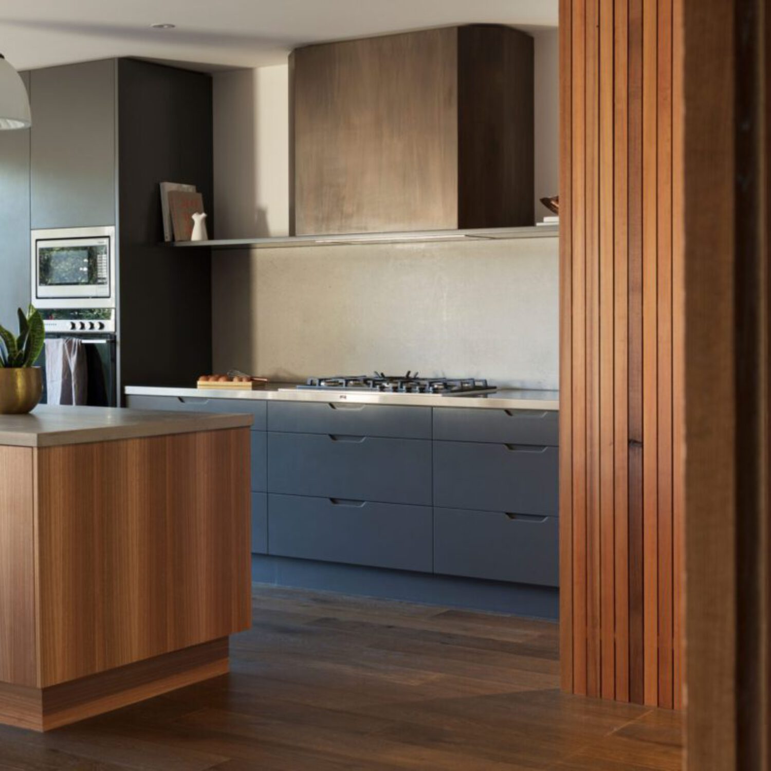 reforma-cocina-moderna-isla Cocina moderna con isla central revestida de piedra, taburetes y muebles altos de madera oscura, reforma de cocina en Madrid